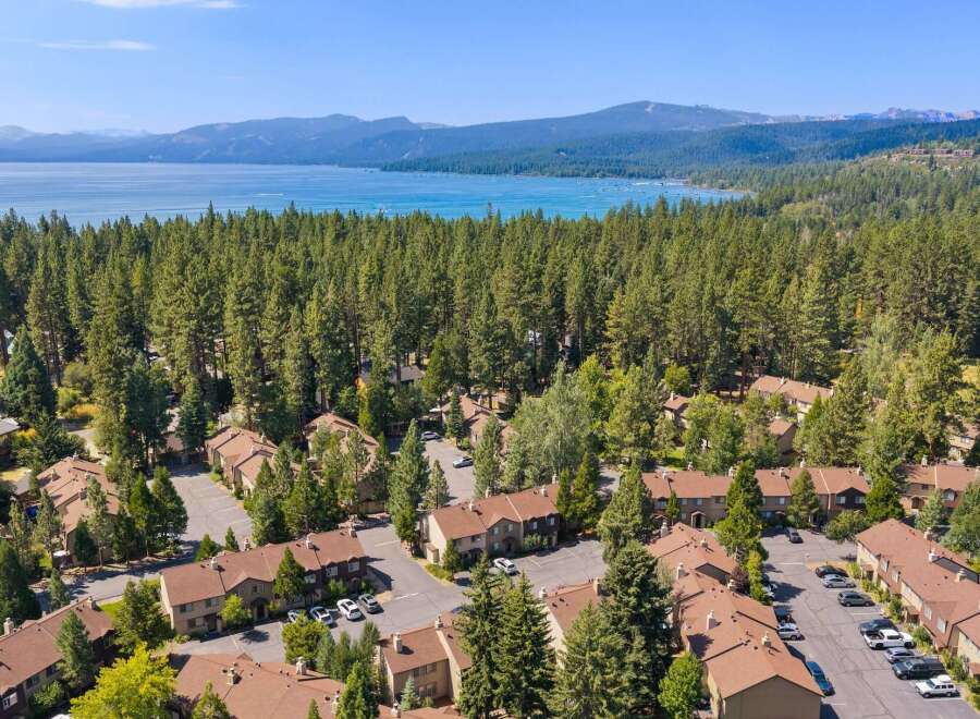 Experience serene living with this stunning aerial view of a lakeside community nestled amongst towering pine trees.