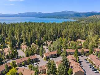 Experience serene living with this stunning aerial view of a lakeside community nestled amongst towering pine trees.