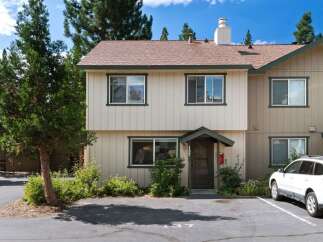 Discover this charming townhouse featuring a light-colored exterior with dark green trim and a classic brown roof.