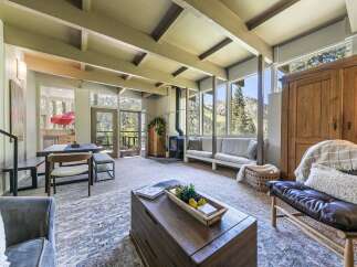 Experience breathtaking mountain views from this stunning living room, featuring a vaulted ceiling with exposed beams and a cozy wood-burning stove.