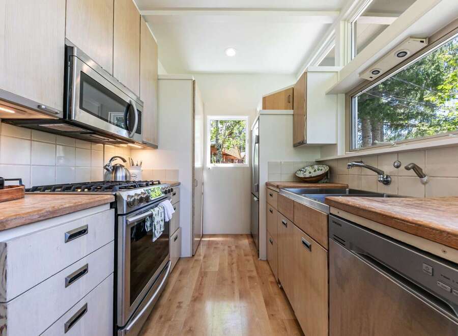 This galley kitchen boasts modern stainless steel appliances, including a microwave and a gas range, complemented by light wood cabinetry and countertops.