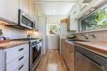 This galley kitchen boasts modern stainless steel appliances, including a microwave and a gas range, complemented by light wood cabinetry and countertops.