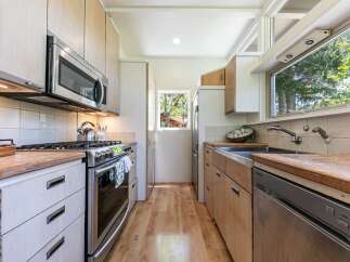 This galley kitchen boasts modern stainless steel appliances, including a microwave and a gas range, complemented by light wood cabinetry and countertops.
