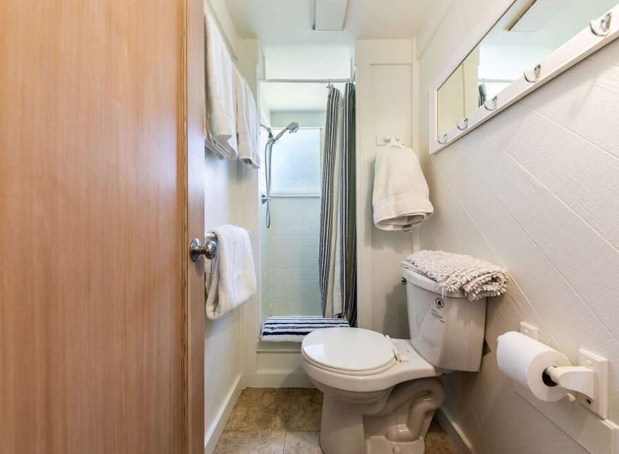 This cozy bathroom features a convenient shower with a striped curtain and a toilet with a plush mat on top.