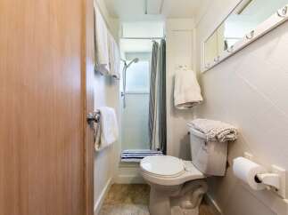 This cozy bathroom features a convenient shower with a striped curtain and a toilet with a plush mat on top.