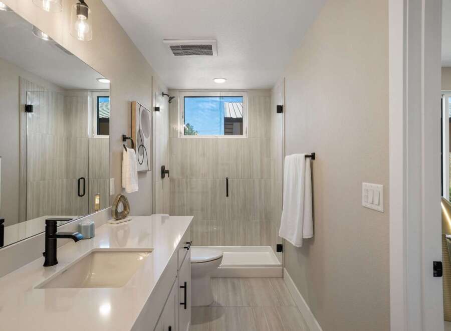This modern bathroom features a sleek vanity with a white countertop and black fixtures, complemented by a spacious glass-enclosed shower with elegant tilework.