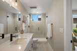 This modern bathroom features a sleek vanity with a white countertop and black fixtures, complemented by a spacious glass-enclosed shower with elegant tilework.