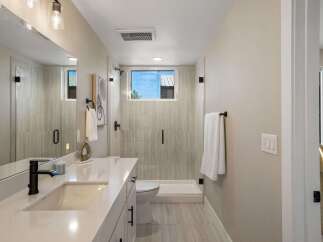 This modern bathroom features a sleek vanity with a white countertop and black fixtures, complemented by a spacious glass-enclosed shower with elegant tilework.