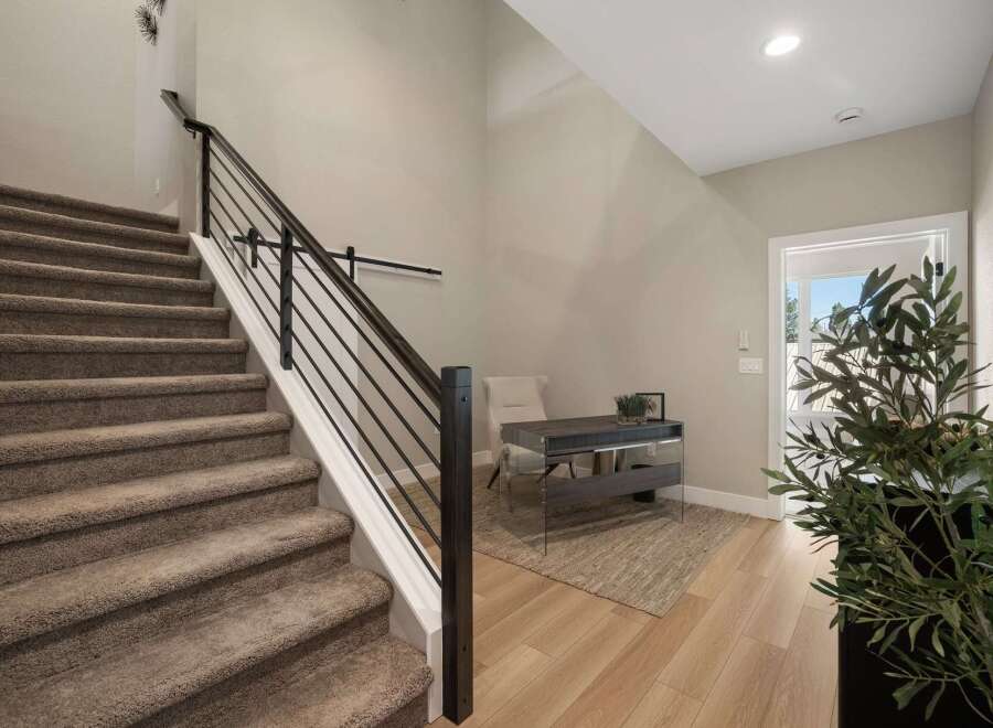 This modern entryway features a carpeted staircase with a sleek black metal railing, leading to an upstairs area.