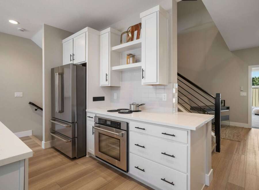 Discover this modern kitchen featuring sleek white cabinetry and stainless steel appliances, including a spacious refrigerator and a built-in oven.