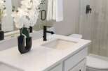 Experience modern elegance in this beautifully appointed bathroom, featuring a sleek white vanity with a quartz countertop and a stylish black faucet.