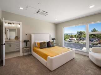 Experience modern comfort in this beautifully appointed bedroom, featuring a plush white bouclé bed and a vibrant yellow quilted comforter.