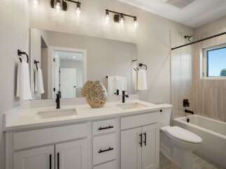 This modern bathroom features a spacious double vanity with white quartz countertops and sleek black fixtures.