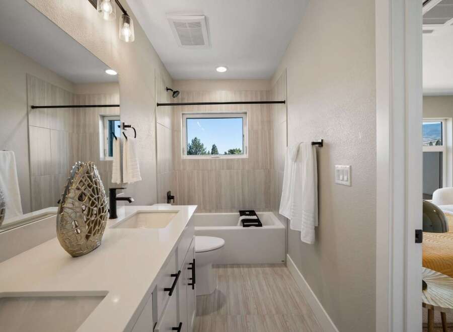 This modern bathroom features a sleek vanity with dual sinks and ample storage, complemented by a spacious bathtub and a large window offering natural light and scenic views.