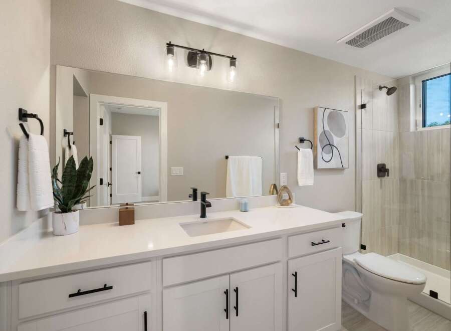 This modern bathroom features a sleek white vanity with black hardware, complemented by a large vanity mirror and a stylish light fixture.