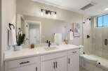 This modern bathroom features a sleek white vanity with black hardware, complemented by a large vanity mirror and a stylish light fixture.