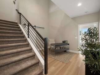 This modern entryway features a carpeted staircase with a sleek black metal railing, leading to an upstairs area.