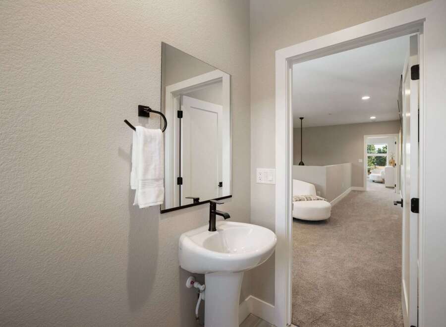 This modern bathroom features a sleek pedestal sink with a black faucet, complemented by a black towel rack holding plush white towels.