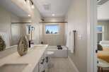 This modern bathroom features a sleek vanity with dual sinks and ample storage, complemented by a spacious bathtub and a large window offering natural light and scenic views.