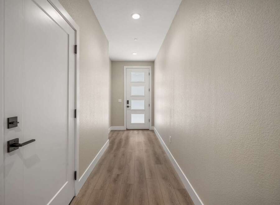 Step into this inviting hallway, featuring a sleek white door with modern black hardware on the left and a charming glass-paneled front door at the end.