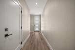 Step into this inviting hallway, featuring a sleek white door with modern black hardware on the left and a charming glass-paneled front door at the end.