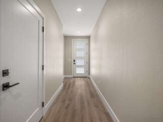 Step into this inviting hallway, featuring a sleek white door with modern black hardware on the left and a charming glass-paneled front door at the end.