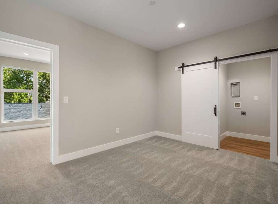 Discover modern living in this spacious room featuring a stylish white barn door leading to a laundry area.