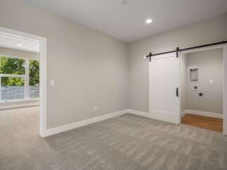 Discover modern living in this spacious room featuring a stylish white barn door leading to a laundry area.
