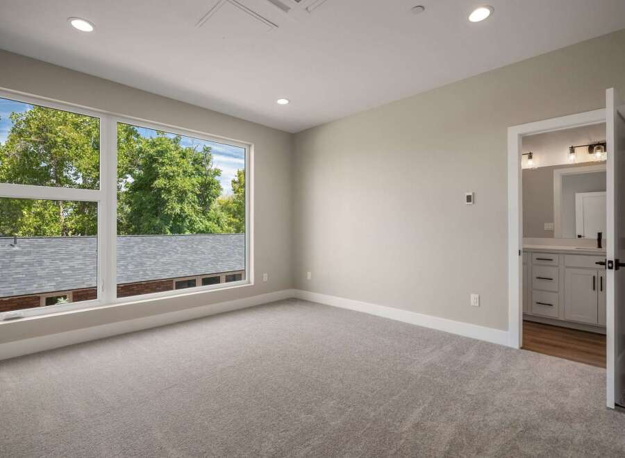 Step into this beautifully appointed bedroom featuring a large picture window that floods the space with natural light and offers serene views of lush greenery.