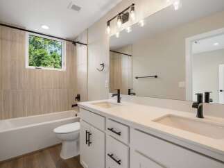 This modern bathroom features a sleek white vanity with dual sinks and black fixtures, complemented by a spacious bathtub and toilet.