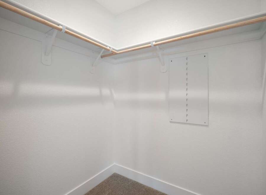 Discover ample storage in this spacious walk-in closet, featuring sturdy wooden rods and white shelving brackets.
