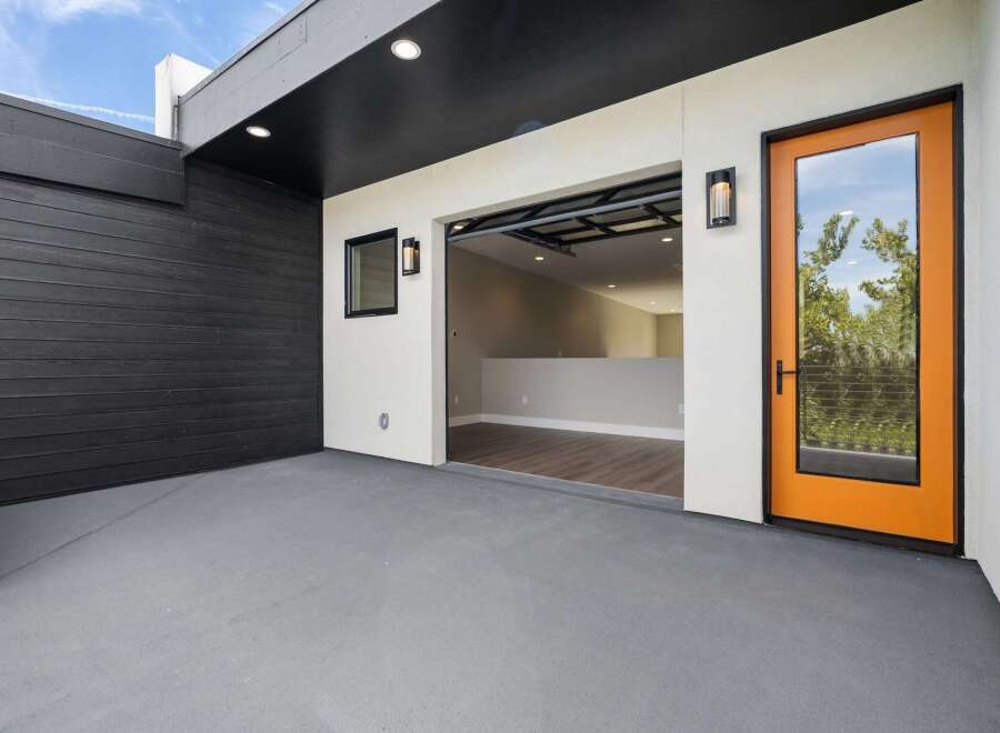 Discover modern living with this stunning property featuring a sleek black wood-paneled exterior and a bright, open-concept interior accessible through a striking orange-framed glass door.