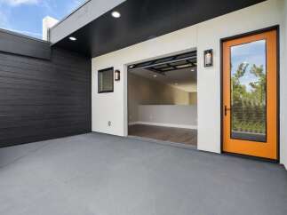 Discover modern living with this stunning property featuring a sleek black wood-paneled exterior and a bright, open-concept interior accessible through a striking orange-framed glass door.