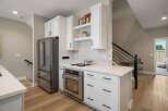 Discover this modern kitchen featuring sleek white cabinetry and stainless steel appliances, including a spacious refrigerator and a built-in oven.