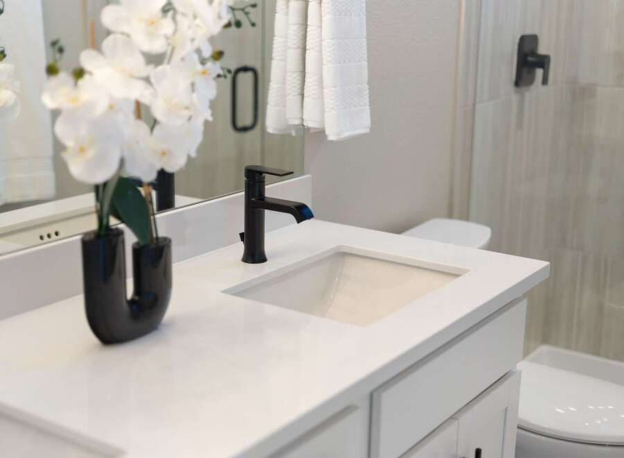 Experience modern elegance in this beautifully appointed bathroom, featuring a sleek white vanity with a quartz countertop and a stylish black faucet.