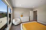 Experience modern comfort in this inviting bedroom, featuring a plush white armchair and a sleek white dresser.