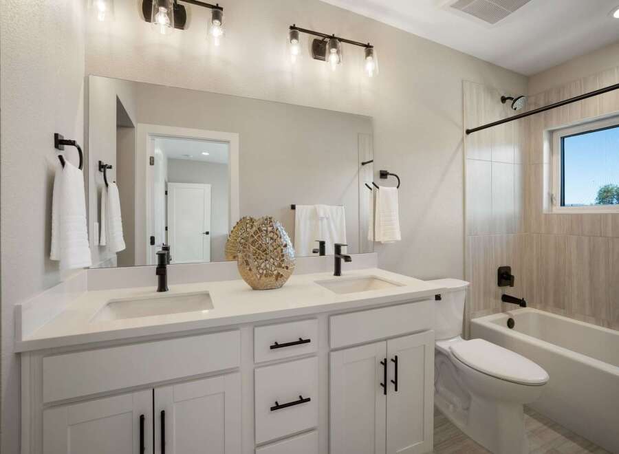 This modern bathroom features a spacious double vanity with white quartz countertops and sleek black fixtures.