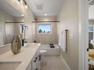 This modern bathroom features a sleek vanity with dual sinks and ample storage, complemented by a spacious bathtub and a large window offering natural light and scenic views.