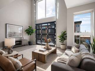 Experience modern living in this stunning living room featuring soaring ceilings and a dramatic floor-to-ceiling glass garage door that opens to the outdoors.
