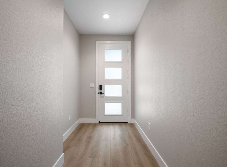 Step into a welcoming entryway featuring a modern white door with frosted glass panels, offering a glimpse of natural light.