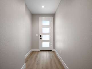 Step into a welcoming entryway featuring a modern white door with frosted glass panels, offering a glimpse of natural light.