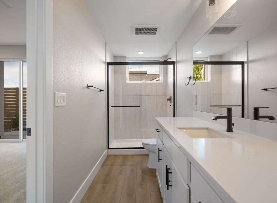 This modern bathroom features a sleek white vanity with black hardware, complemented by a spacious walk-in shower with elegant tilework.
