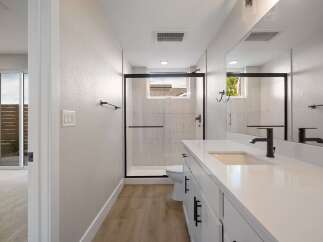 This modern bathroom features a sleek white vanity with black hardware, complemented by a spacious walk-in shower with elegant tilework.