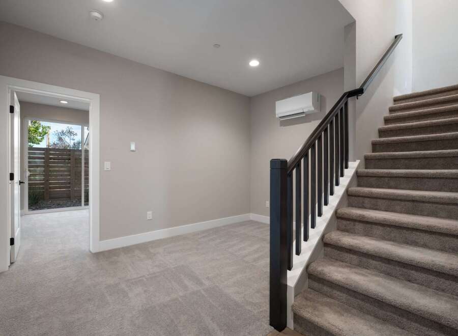 This spacious interior features a modern staircase with dark wood railings and plush carpeting, leading to the upper level.