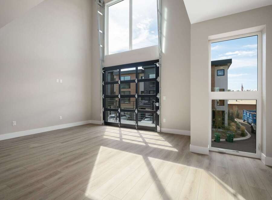 Experience modern living in this spacious room featuring a dramatic floor-to-ceiling glass garage door that opens to the outdoors.