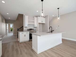 Discover modern living in this stunning kitchen featuring sleek white cabinetry, a spacious island with a contemporary faucet, and elegant pendant lighting.