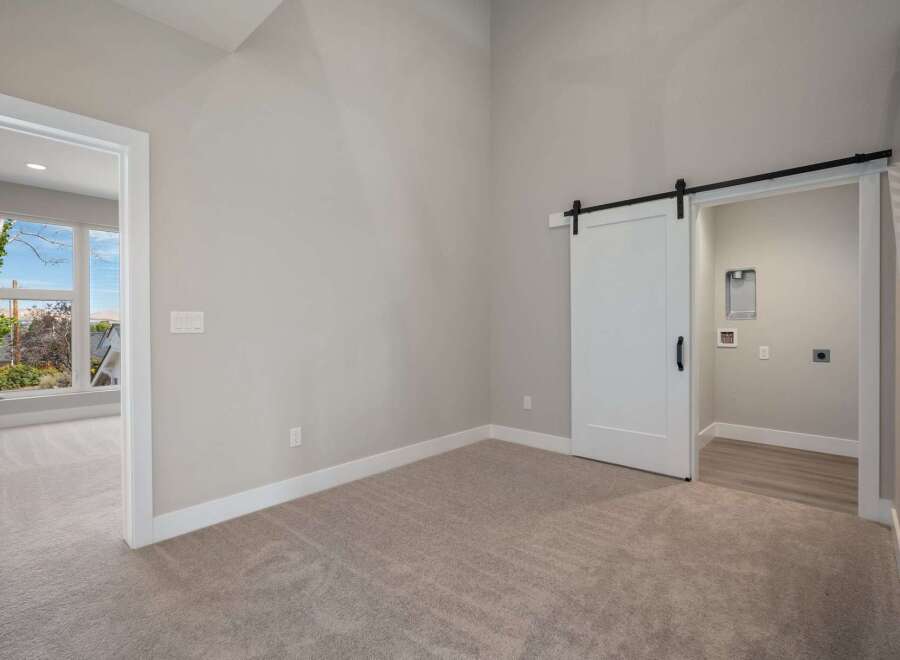Discover modern living with this spacious room featuring a stylish white barn door leading to a convenient laundry area.