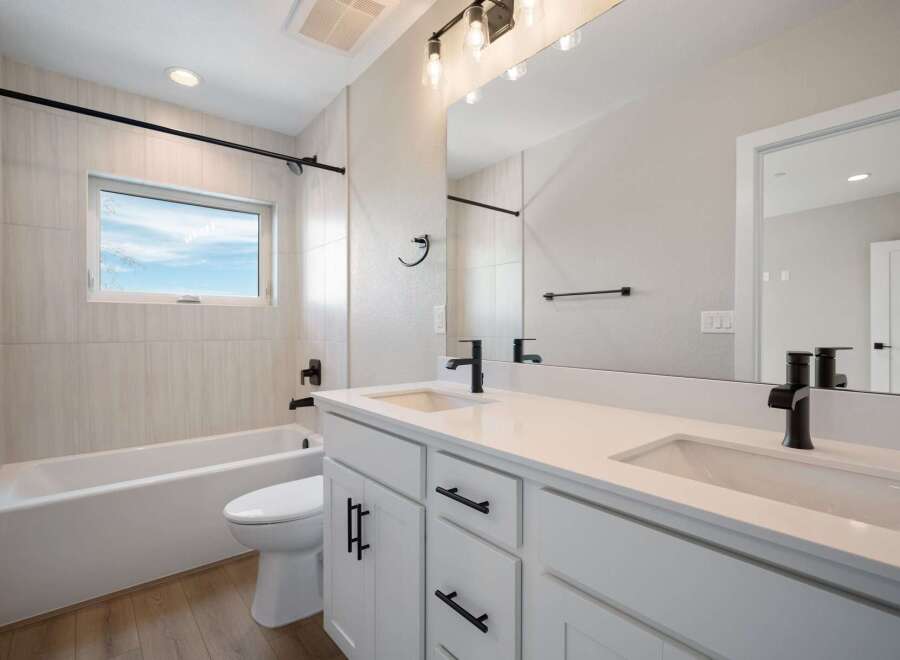 This modern bathroom features a sleek white vanity with dual sinks and black fixtures, complemented by a spacious bathtub and toilet.