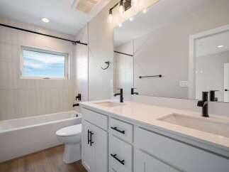 This modern bathroom features a sleek white vanity with dual sinks and black fixtures, complemented by a spacious bathtub and toilet.