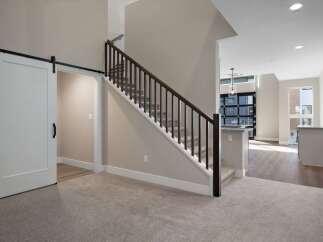 Experience modern living in this stunning home featuring a sleek barn door leading to a private space and a beautifully carpeted staircase with dark wood railings.